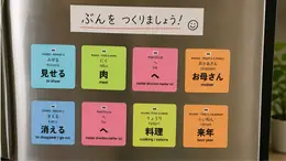 Eight JLPT vocabulary stickers on a refrigerator door under a handwritten note, including 見せる (miseru, to show), 肉 (niku, meat), and お母さん (okaasan, mother)