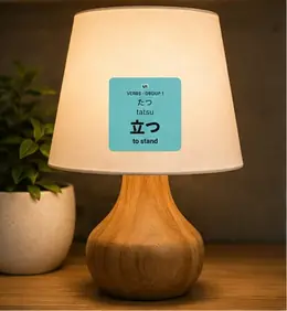 A 立つ (tatsu, to stand) JLPT verb sticker on a wooden table lamp base
