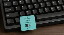 A 座る (suwaru, to sit) vocabulary sticker resting on a mechanical keyboard