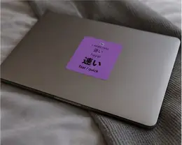 A 速い (hayai, fast/quick) vocabulary sticker on the lid of a laptop resting on a bed