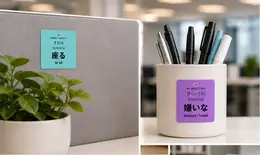 Two JLPT vocabulary stickers in an office: 座る (suwaru, to sit) on a cubicle divider and 嫌いな (kirai[na], disliked) on a pen cup