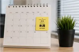A 来週 (raishuu, next week) vocabulary sticker on a desk calendar next to a potted plant