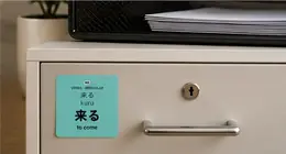 A 来る (kuru, to come) vocabulary sticker on a filing cabinet drawer